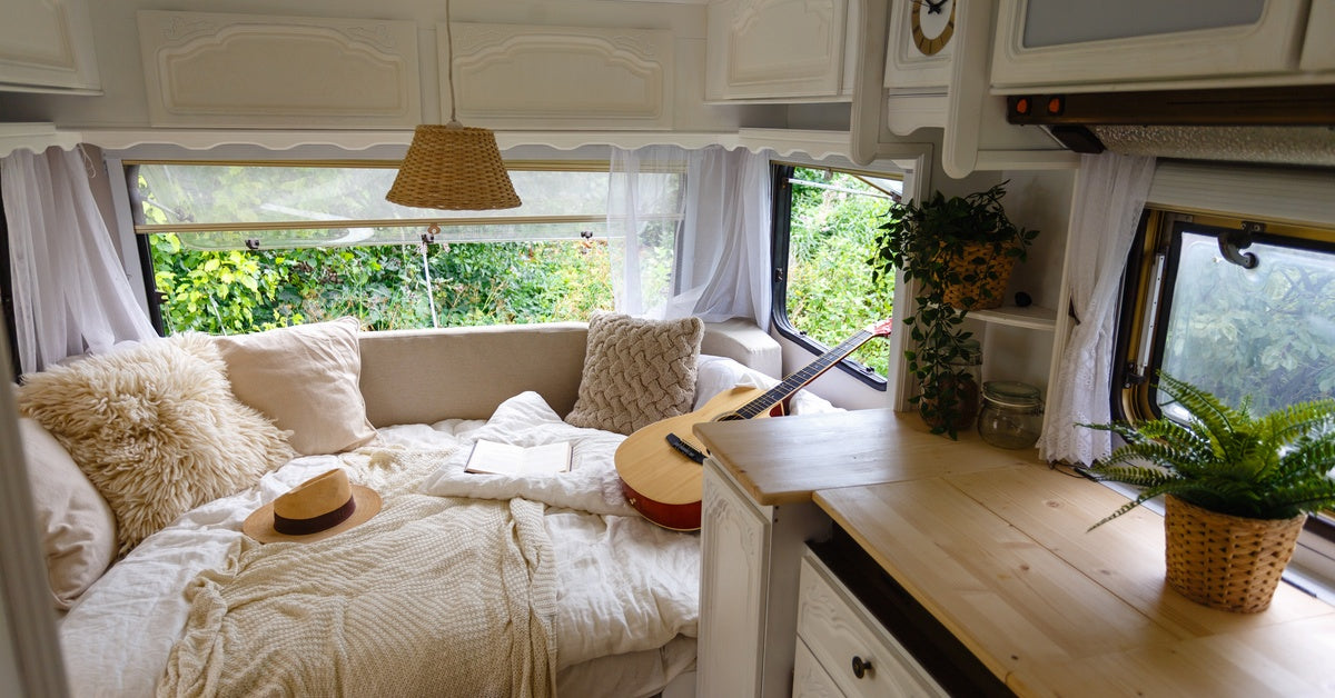 The inside of an RV. The bed has several throw pillows on it and small plants decorate the kitchen cabinet.