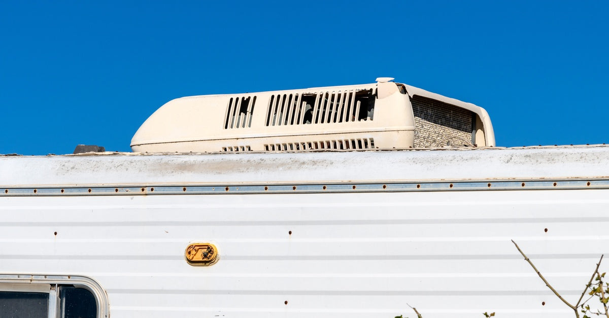 A rooftop AC unit on top of an older white camper. Some of the parts appear worn down and covered in dirt.