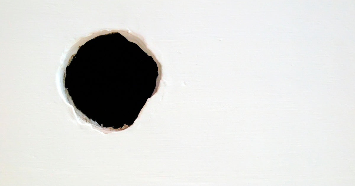 A close-up of a large, circular hole in what looks like plaster, with complete darkness visible beyond it.